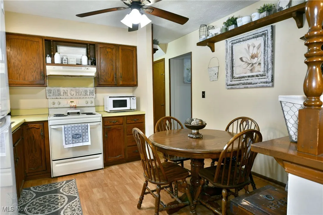 Kitchen featuring open shelves, white appliances, light countertops, light wood-type flooring, and under cabinet range hood