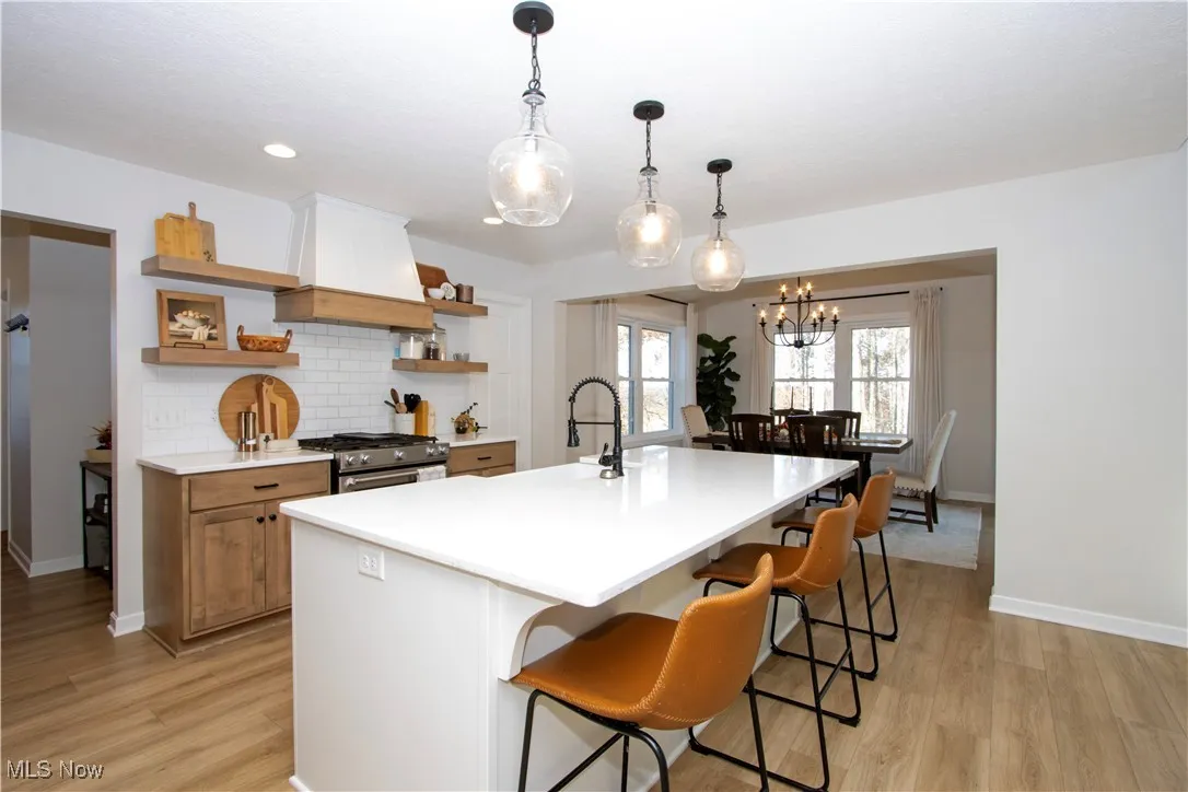 Kitchen featuring tasteful backsplash, custom exhaust hood, high end stove, hanging light fixtures, and light wood finished floors