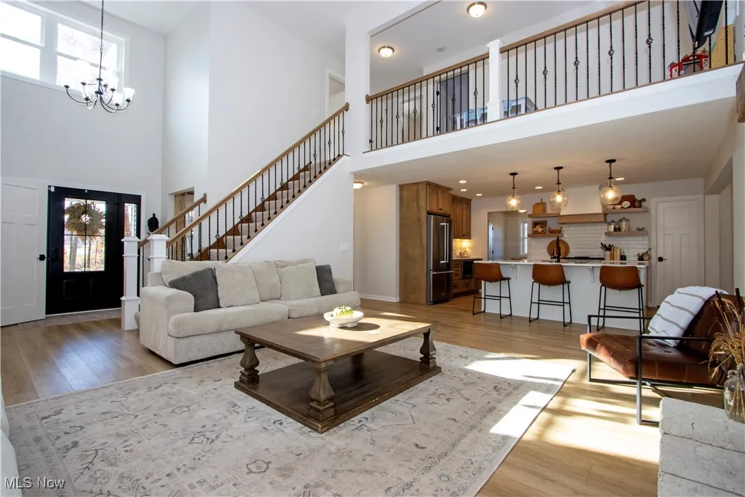 Living area featuring a high ceiling, stairs, light wood finished floors, a chandelier, and recessed lighting