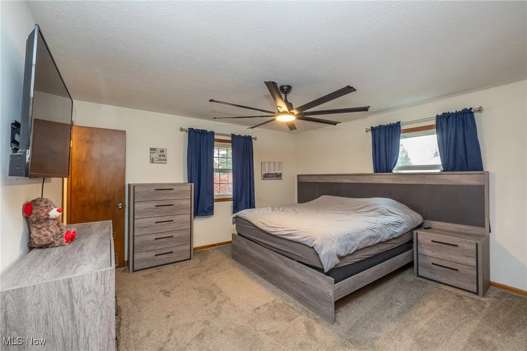 Bedroom featuring light carpet, multiple windows, a ceiling fan, and a textured ceiling