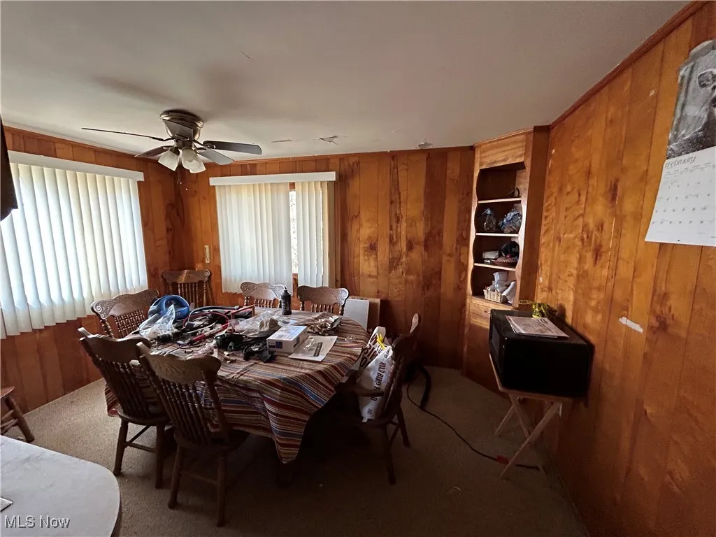 Dining area featuring wooden walls, carpet flooring, and a ceiling fan