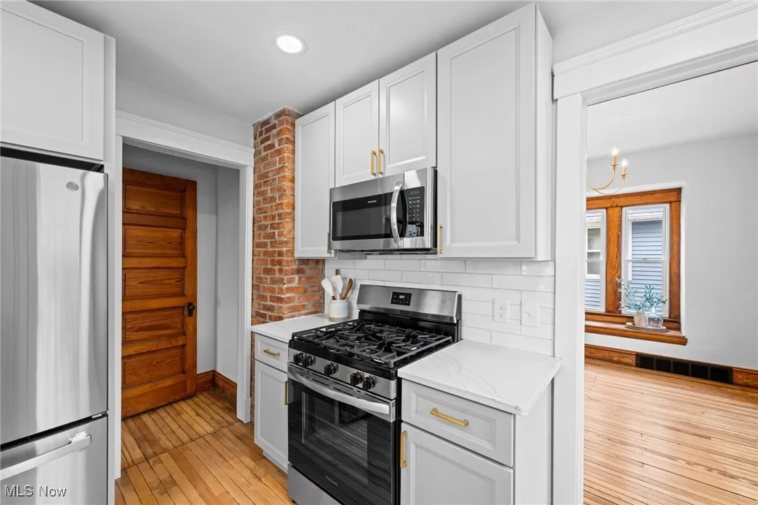 Kitchen featuring stainless steel appliances, white cabinetry, light wood floors, and a light stone countertops