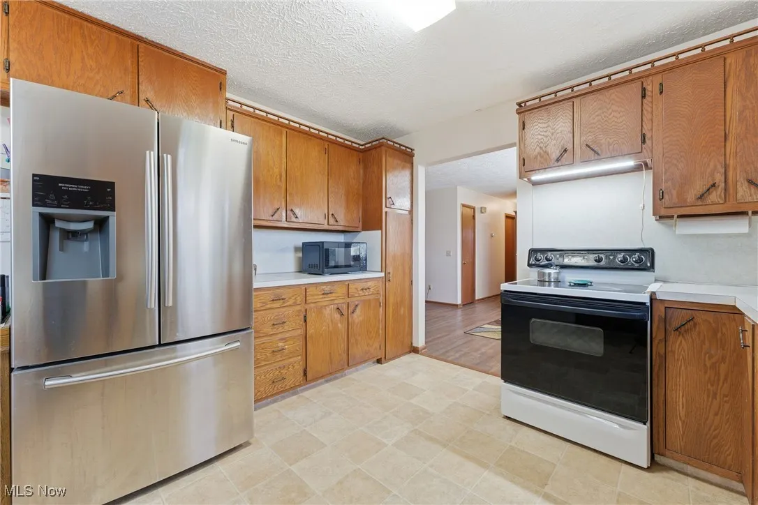 Kitchen featuring stainless steel fridge with ice dispenser, electric range oven, light countertops, a textured ceiling, and black microwave