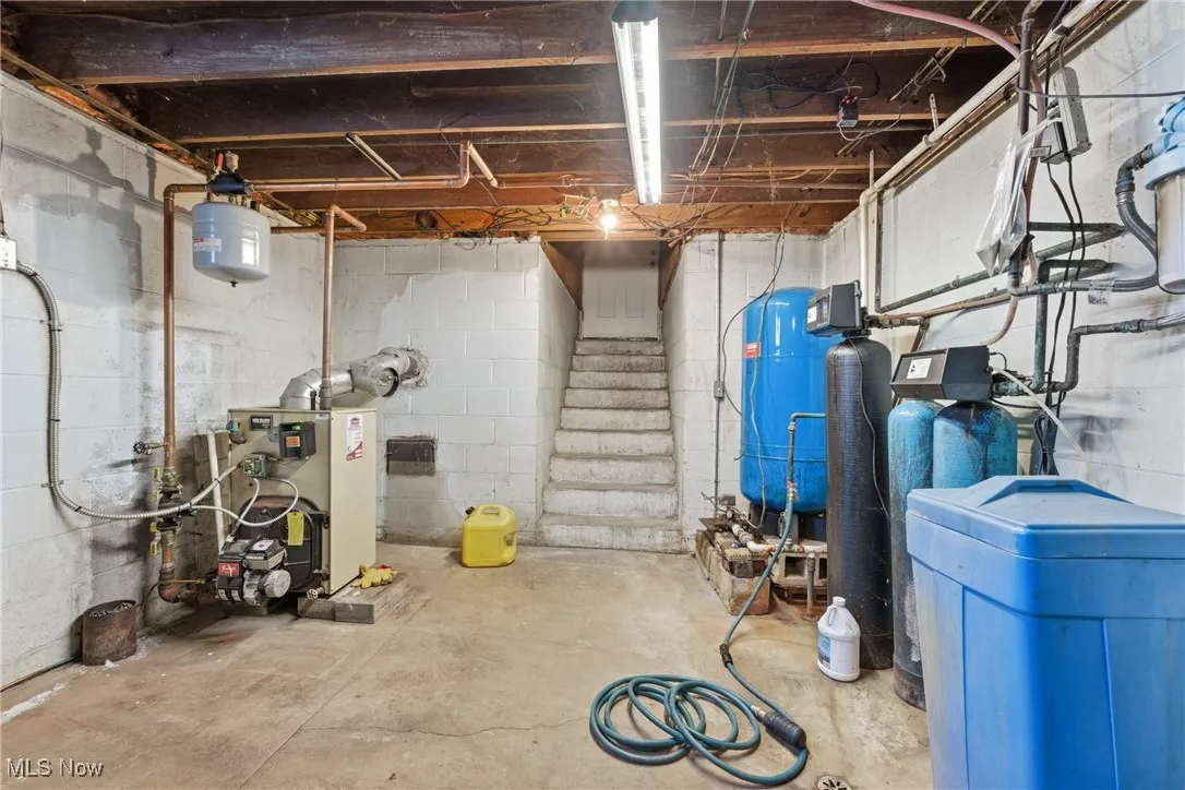 Unfinished below grade area with a water softener system, stairs, a water pressure tank, and a heating unit