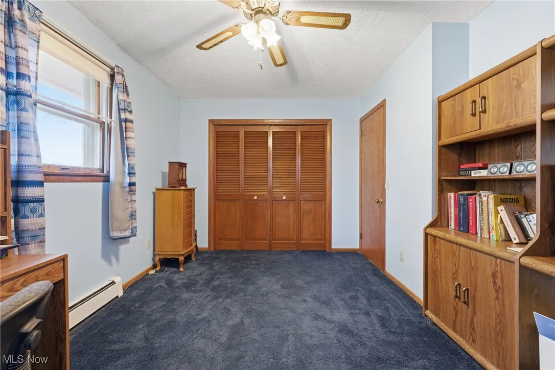 Bedroom with baseboard heating, dark colored carpet, a closet, ceiling fan, and a textured ceiling