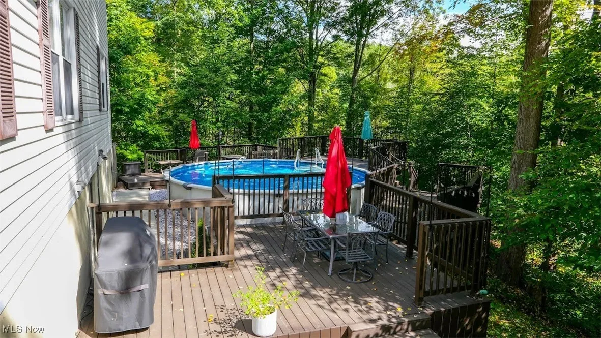 Wooden terrace with outdoor dining space, an outdoor pool, and grilling area