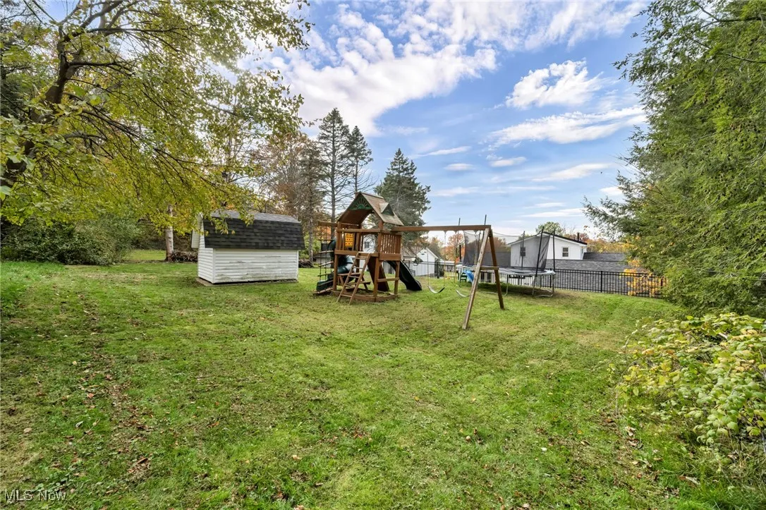 View of yard with a trampoline, a playground, and a storage shed