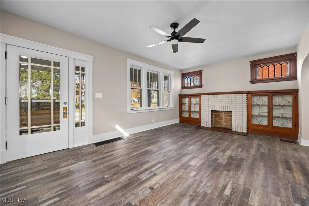 Unfurnished living room featuring a brick fireplace, dark wood finished floors, and ceiling fan