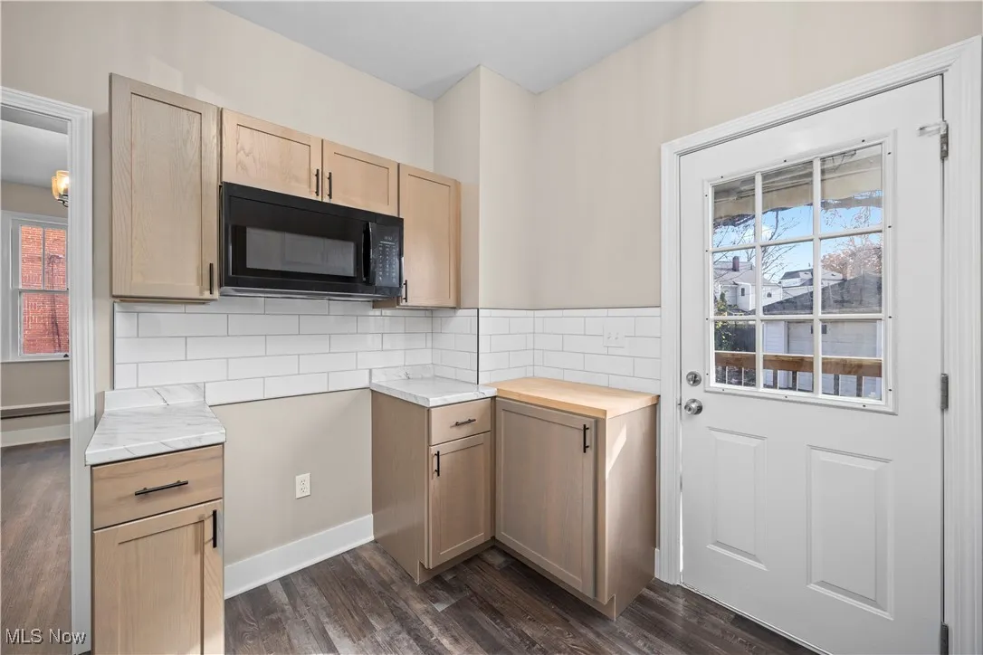 Kitchen featuring black microwave, dark wood-type flooring, and light brown cabinets