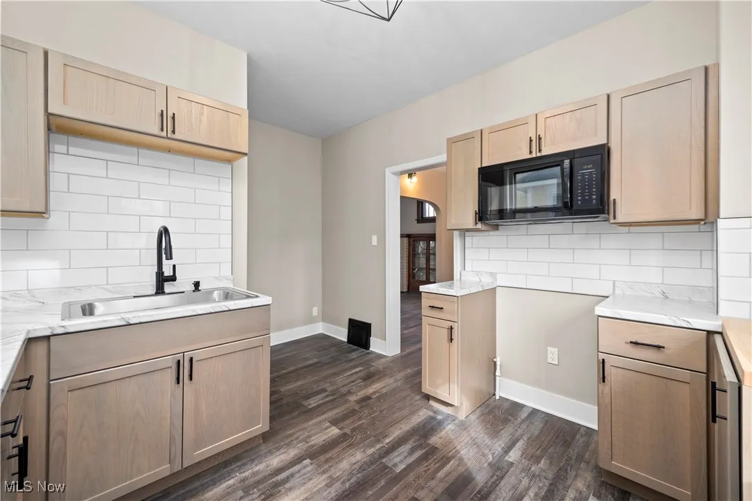 Kitchen featuring tasteful backsplash, light brown cabinets, black microwave, and dark wood-style floors