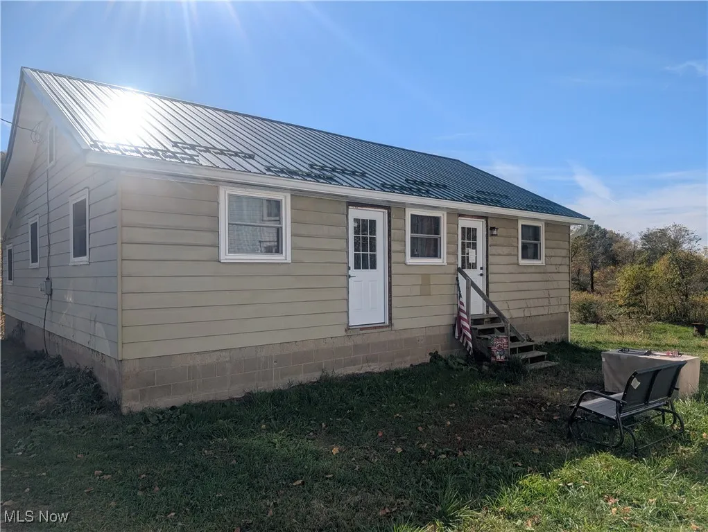 Rear view of property with entry steps, a metal roof, and a lawn
