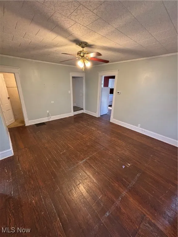 Unfurnished room with dark wood-style floors, ceiling fan, and ornamental molding