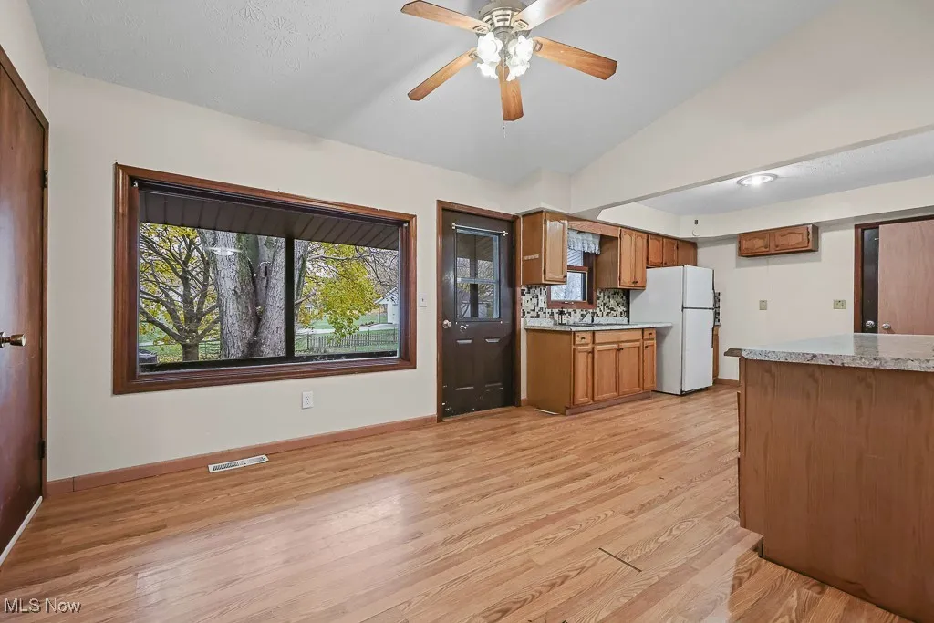 Kitchen featuring brown cabinets, light countertops, light wood-type flooring, freestanding refrigerator, and vaulted ceiling