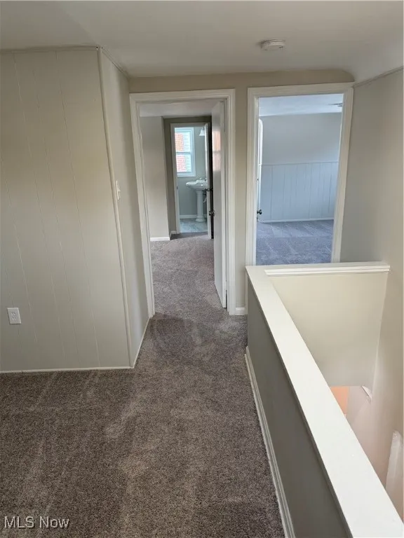 Hallway featuring dark carpet and an upstairs landing