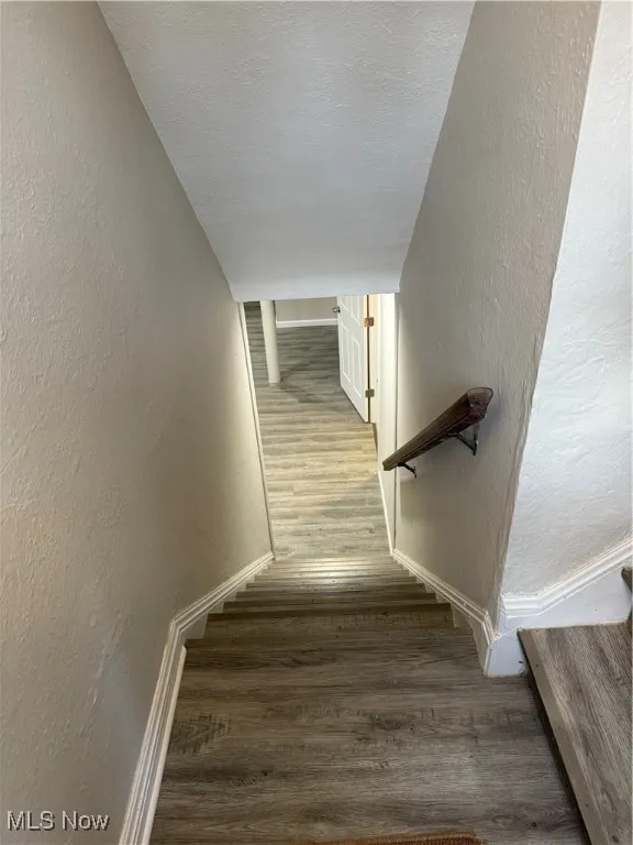 Staircase featuring a textured wall, wood finished floors, and a textured ceiling