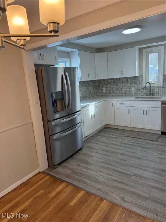 Kitchen featuring white cabinets, stainless steel fridge, light wood-style flooring, and backsplash