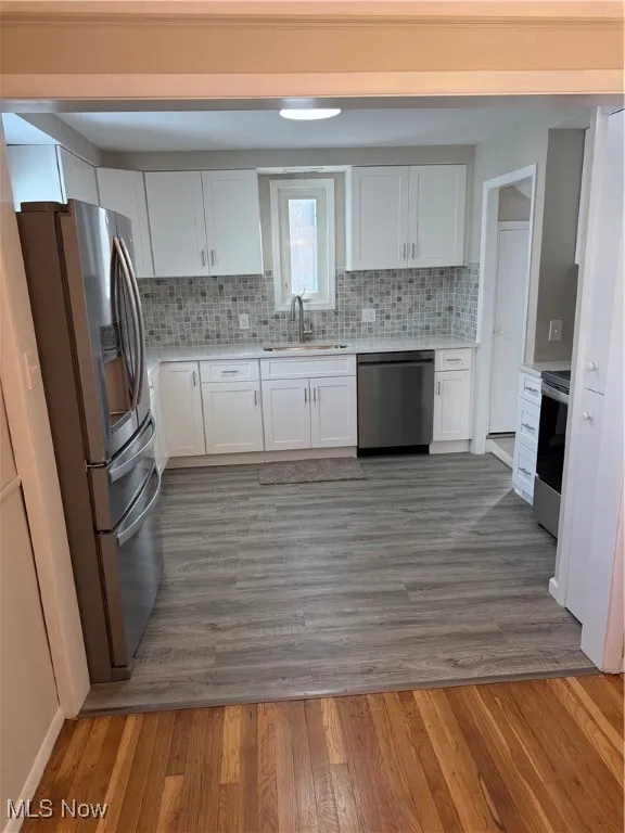 Kitchen featuring white cabinets, light wood-style floors, stainless steel refrigerator, and dishwashing machine