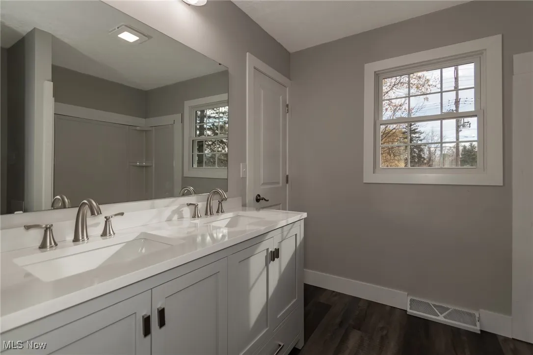 Full bath with double vanity and dark wood-type flooring