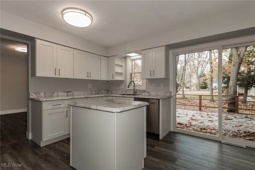Kitchen featuring white cabinetry, dark wood-type flooring, stainless steel dishwasher, a center island, and light stone countertops
