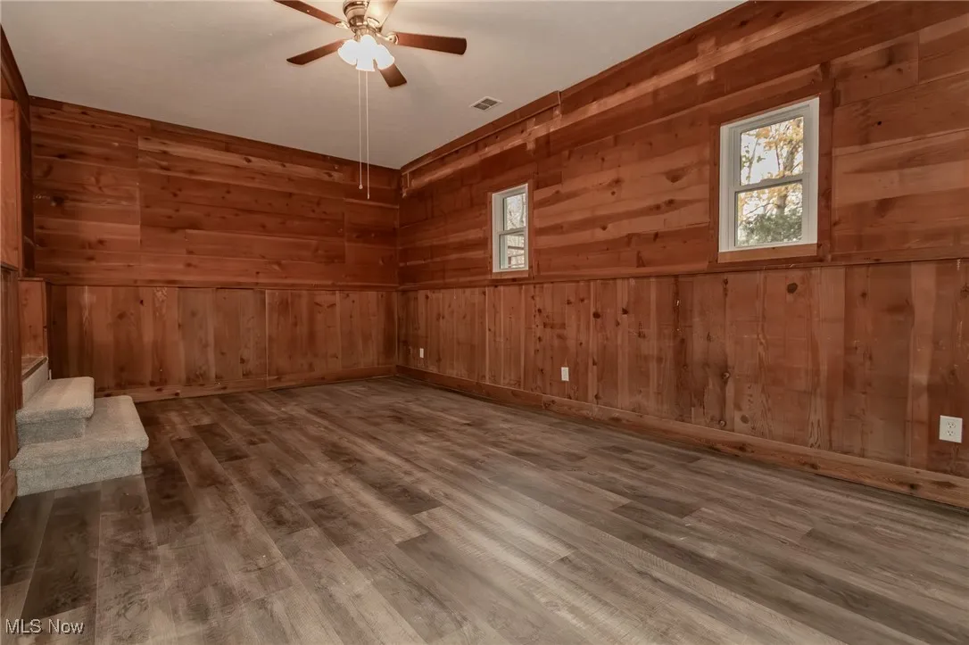 Unfurnished room featuring wooden walls, wood finished floors, and stairway