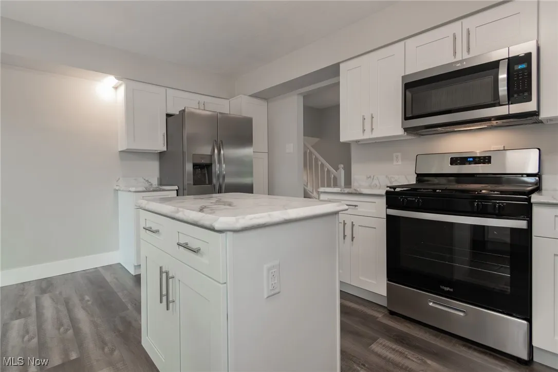 Kitchen featuring appliances with stainless steel finishes, white cabinetry, dark wood finished floors, a center island, and light stone countertops