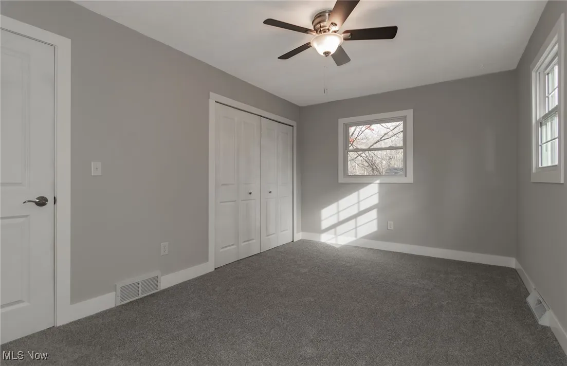 Unfurnished bedroom featuring carpet flooring, multiple windows, ceiling fan, and a closet