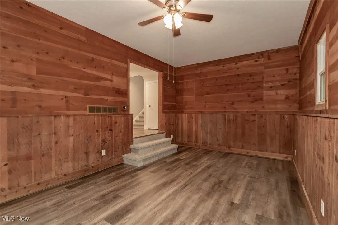 Empty room with wood finished floors, stairway, wood walls, and a ceiling fan