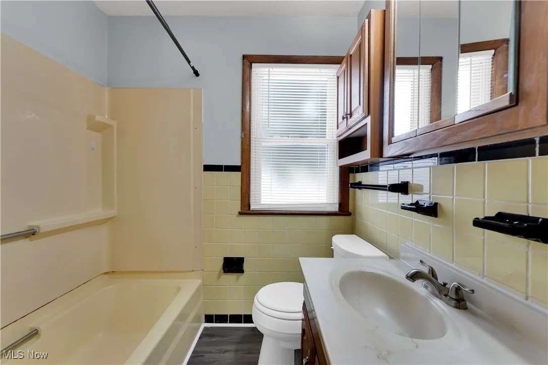 Full bath featuring vanity, tile walls, shower / bathtub combination, and dark wood-type flooring