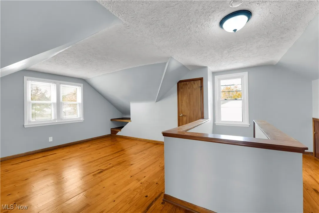 Additional living space featuring lofted ceiling, light wood-style floors, and a textured ceiling