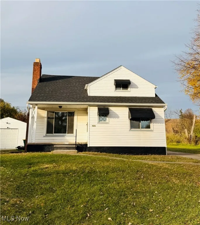 View of front of property with a front yard, a shingled roof, a chimney, and an outbuilding