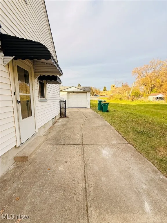 View of side of home featuring a detached garage, a lawn, an outbuilding, and a patio