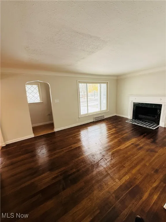 Unfurnished living room with arched walkways, a premium fireplace, dark wood-style floors, plenty of natural light, and a textured ceiling