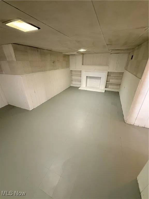 Finished below grade area with tile patterned floors, wood walls, and a fireplace with raised hearth