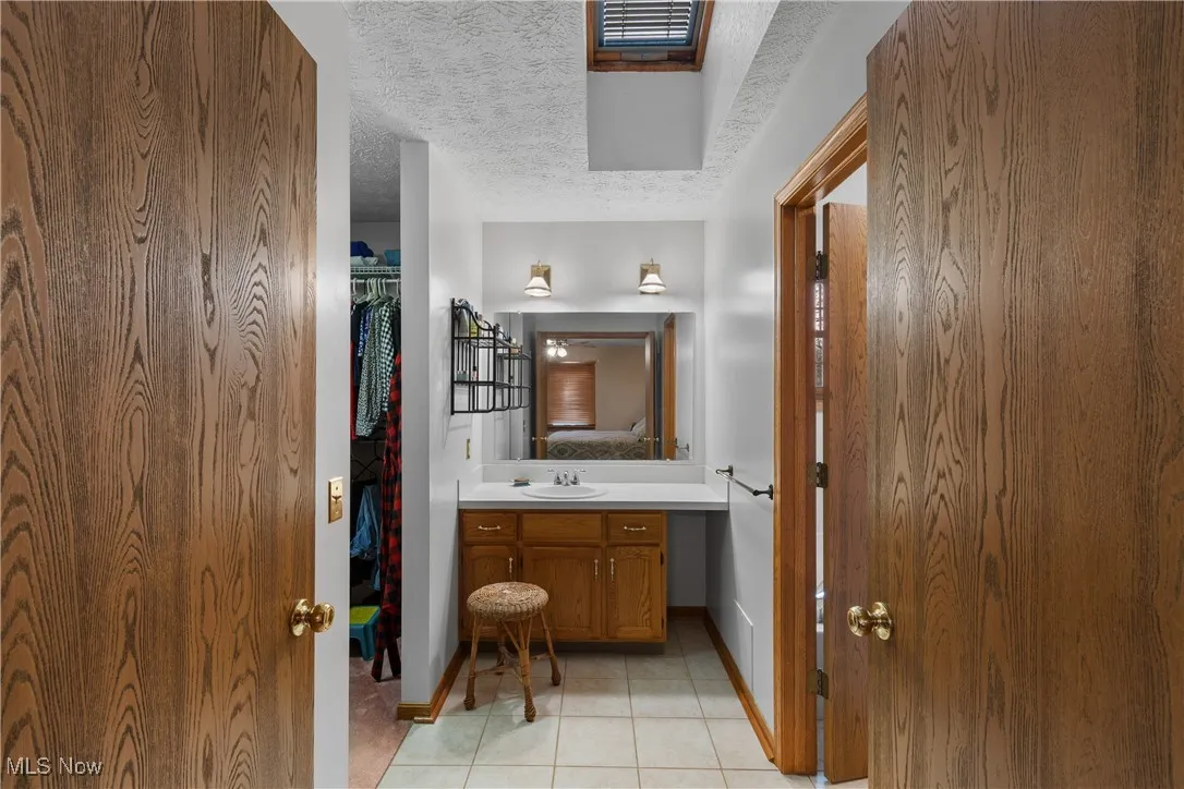 Bathroom featuring vanity, a textured ceiling, light tile patterned floors, a spacious closet, and ensuite bath