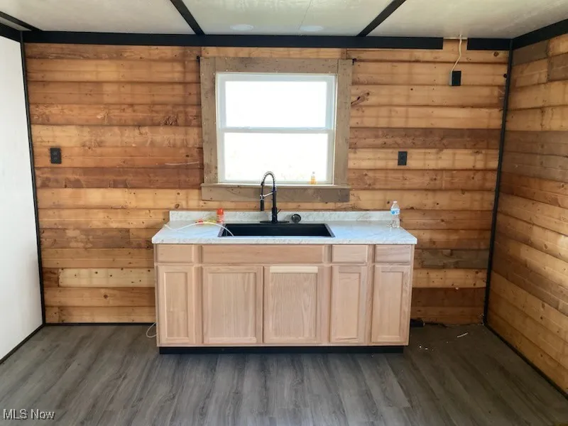 Kitchen with wooden walls, light brown cabinets, light countertops, and dark wood finished floors