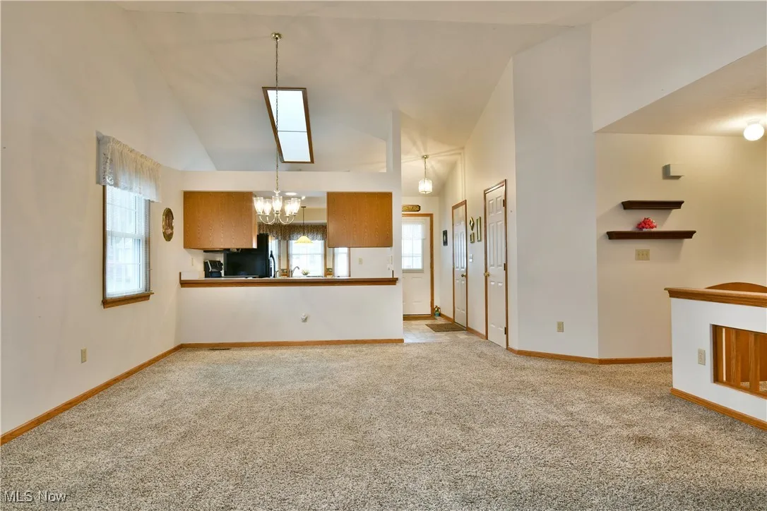 Unfurnished living room with light carpet, high vaulted ceiling, and a chandelier
