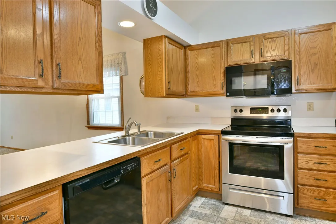 Kitchen with black appliances, light countertops, brown cabinetry, light stone finish flooring, and recessed lighting