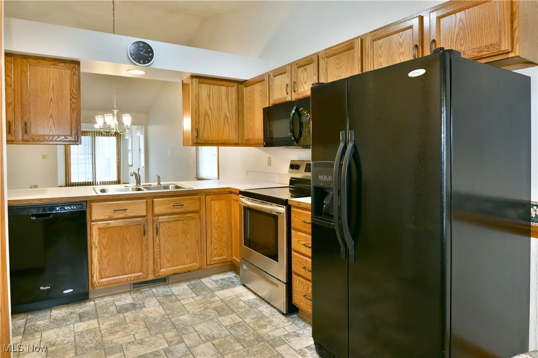 Kitchen featuring black appliances, light countertops, a chandelier, stone finish floors, and brown cabinets