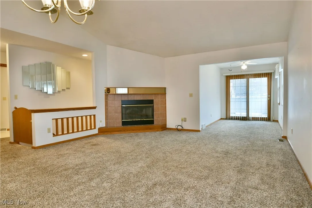 Unfurnished living room featuring a tile fireplace, carpet, a chandelier, and a ceiling fan