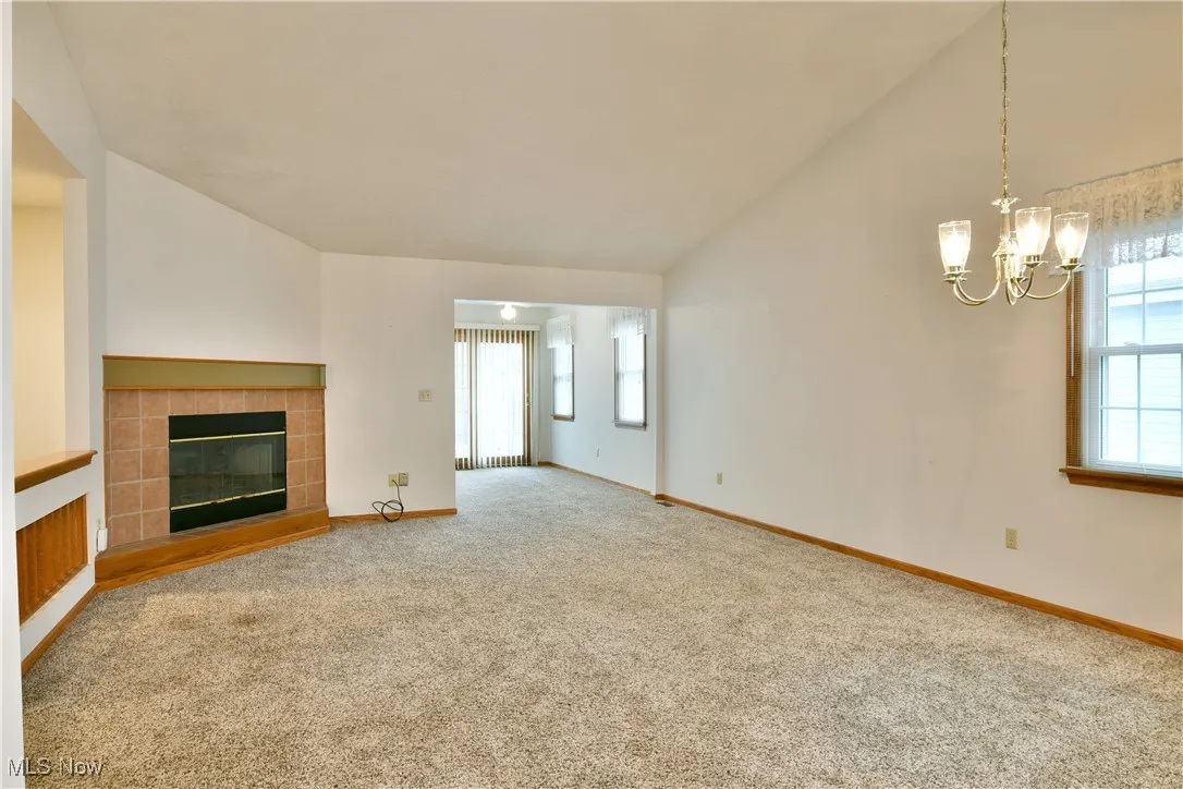 Unfurnished living room featuring a tile fireplace, carpet flooring, healthy amount of natural light, a chandelier, and high vaulted ceiling