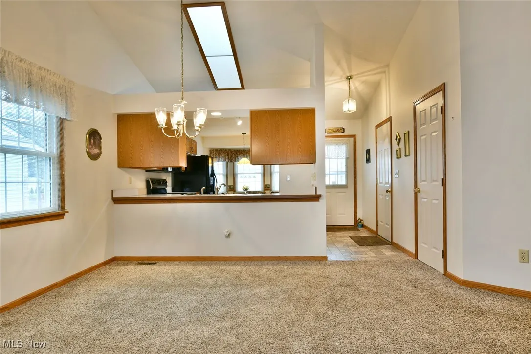 Kitchen with light carpet, a skylight, brown cabinets, decorative light fixtures, and a chandelier