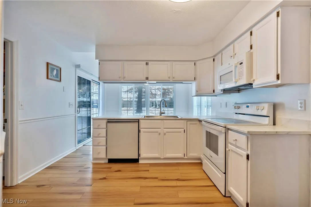 Kitchen with white appliances, white cabinetry, light wood-style flooring, and a peninsula