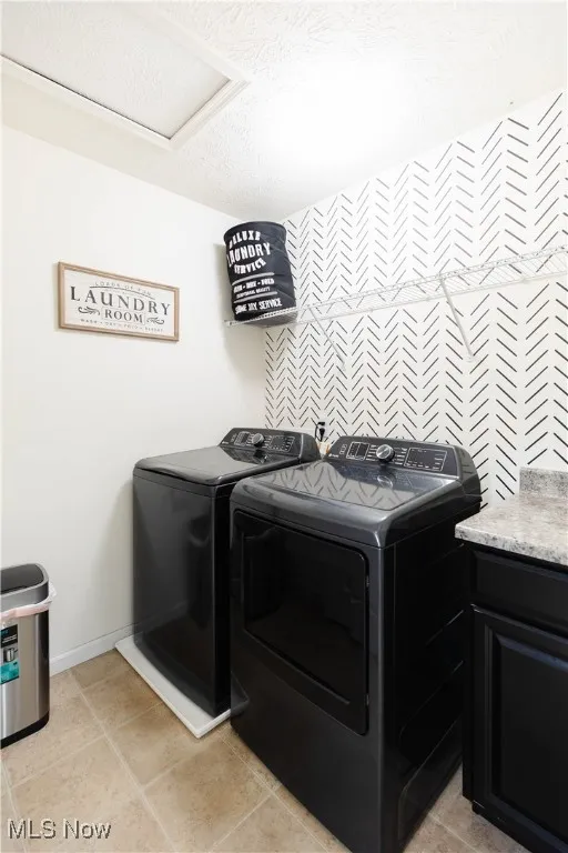 Washroom with a textured ceiling, light tile patterned floors, and washer and dryer