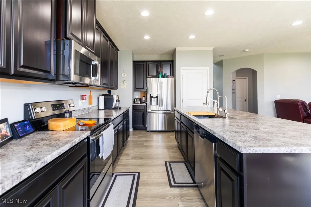 Kitchen featuring appliances with stainless steel finishes, arched walkways, light wood-type flooring, recessed lighting, and light countertops