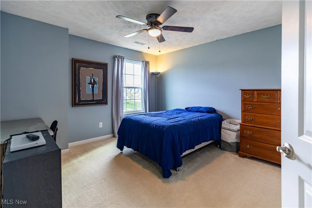 Bedroom featuring light carpet, a textured ceiling, a ceiling fan, and an office area