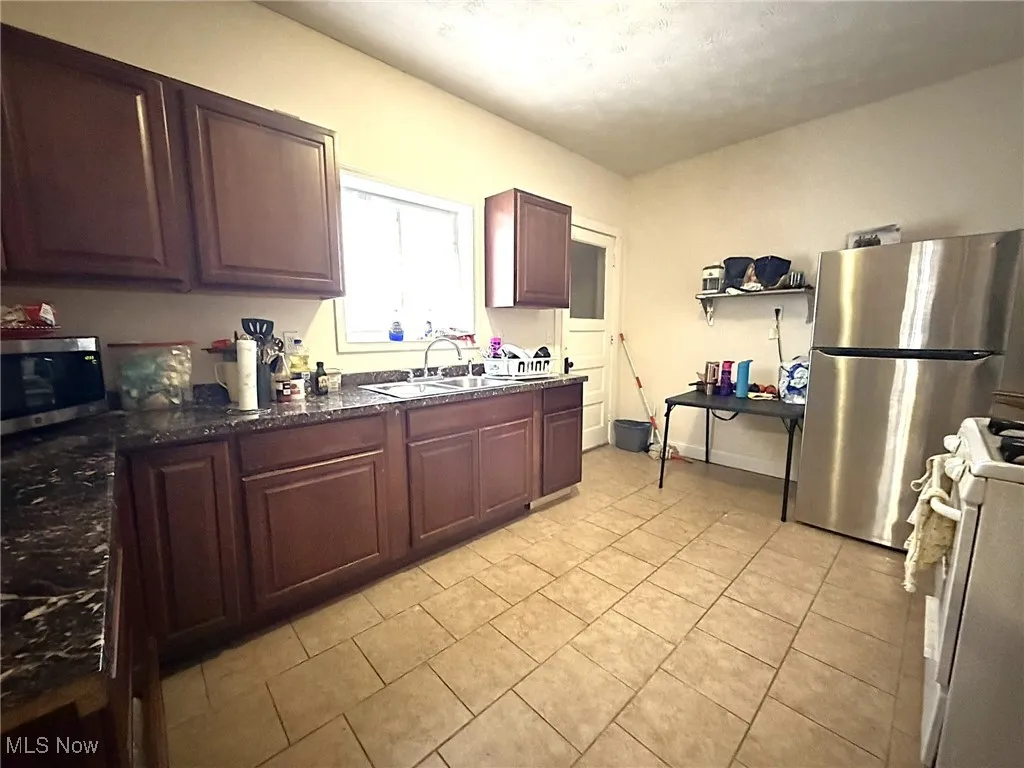 Kitchen with white gas range, dark brown cabinetry, stainless steel microwave, light tile patterned floors, and dark stone counters
