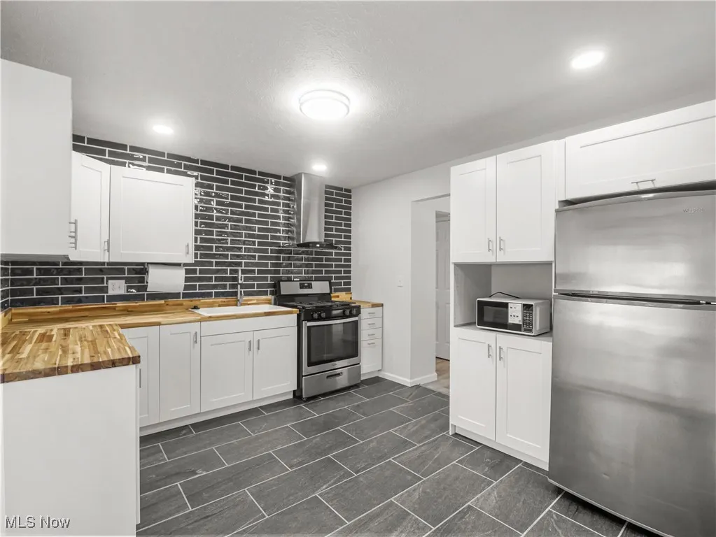 Kitchen featuring stainless steel appliances, wooden counters, backsplash, white cabinets, and a textured ceiling