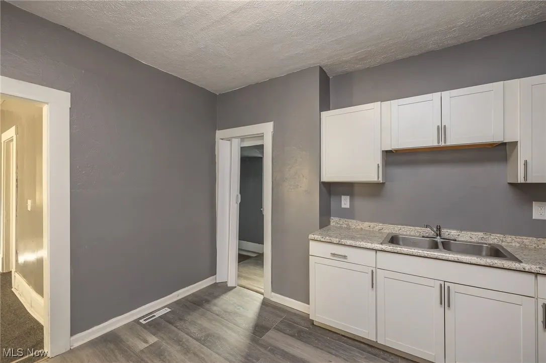 Kitchen with white cabinets, a textured ceiling, dark wood-style flooring, and light stone countertops