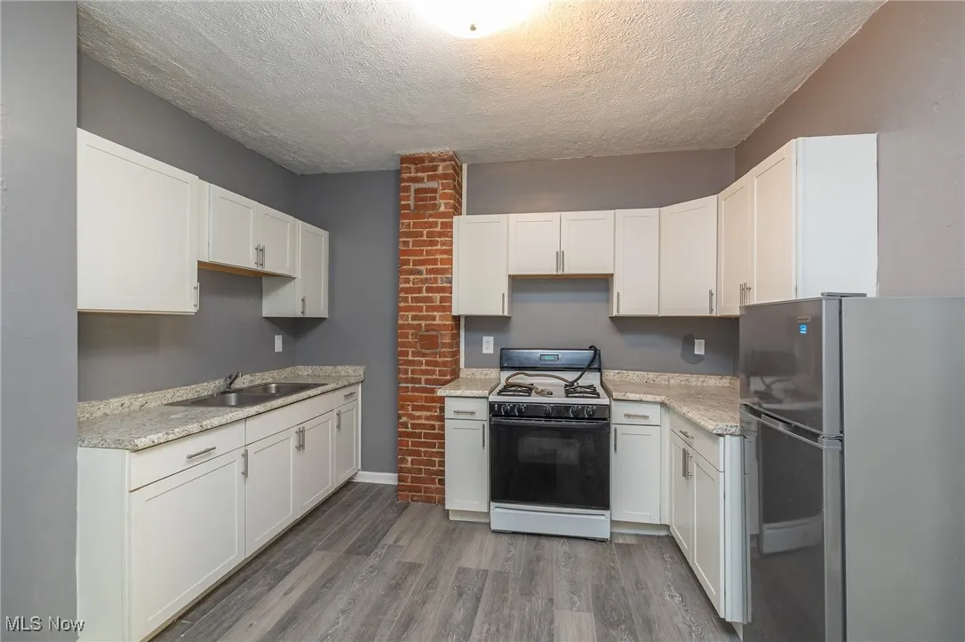 Kitchen with freestanding refrigerator, gas stove, dark wood-style flooring, a textured ceiling, and white cabinets