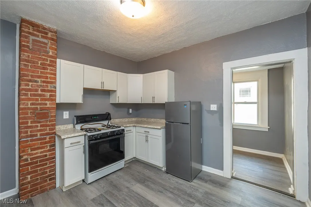 Kitchen featuring range with gas cooktop, freestanding refrigerator, white cabinets, light wood-type flooring, and a textured ceiling